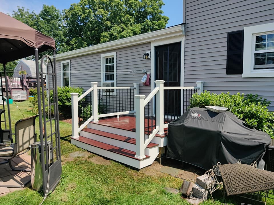 A mobile home with a deck and stairs in front of it.