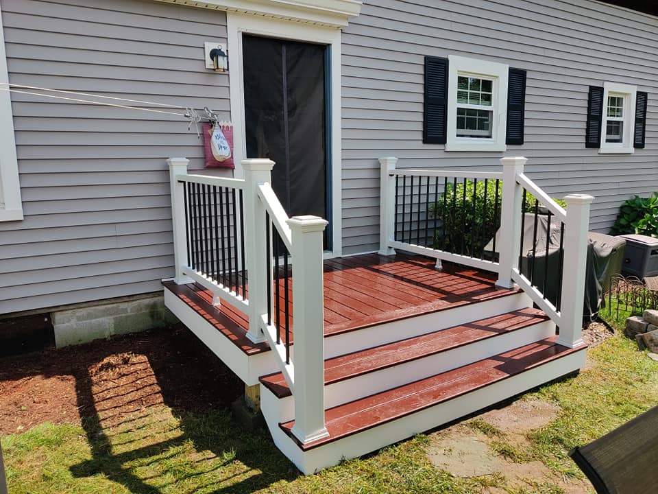 A wooden deck with stairs and a white railing is in front of a house.