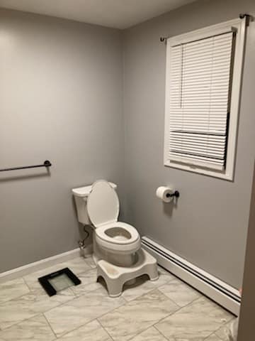 A bathroom with a toilet , scale and window.