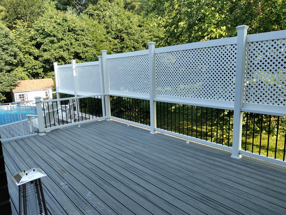 A deck with a white lattice fence and a pool in the background