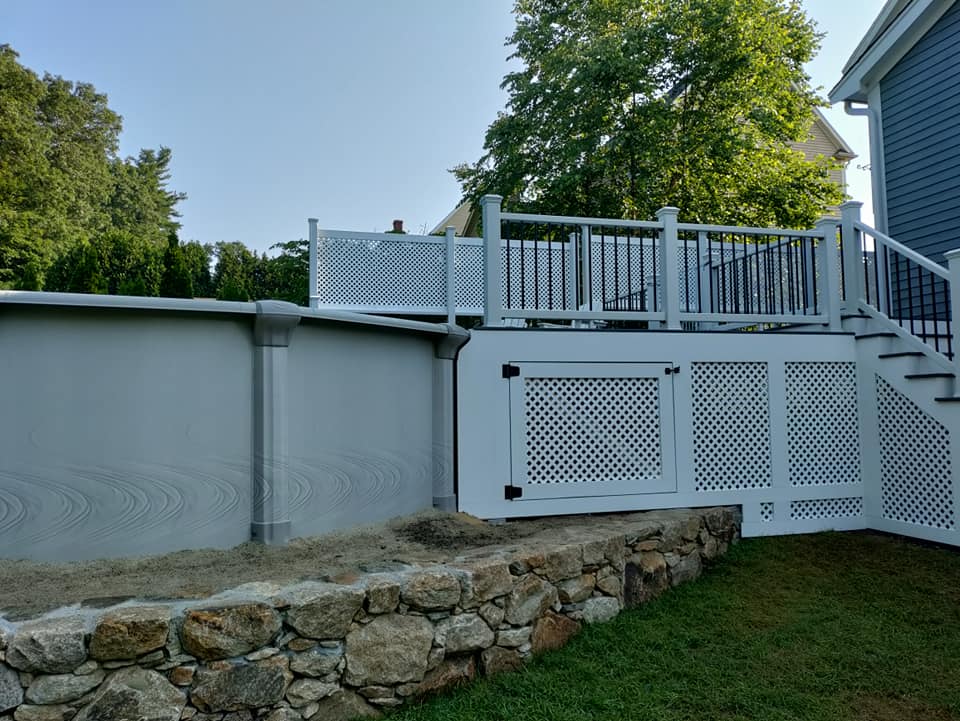 A white deck with stairs and a stone wall next to a house.