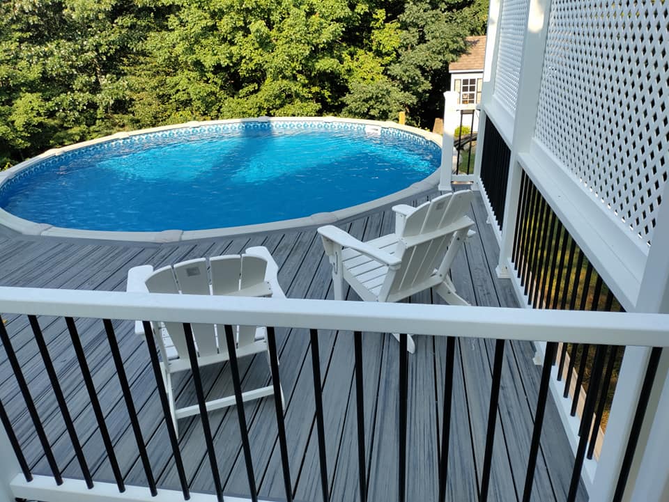 A swimming pool on top of a deck with chairs and a table.