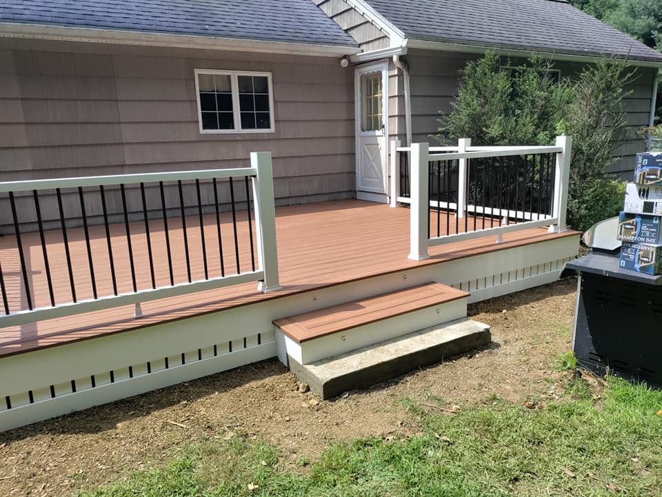 A deck with stairs and a white railing is in front of a house.