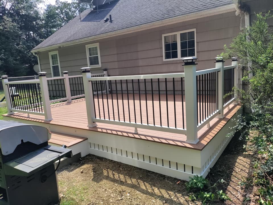 A large deck with a white railing is in front of a house.