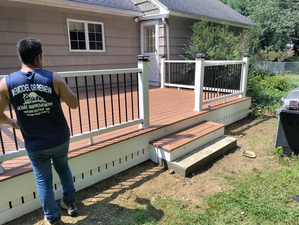 A man in a blue tank top is standing on a deck in front of a house.