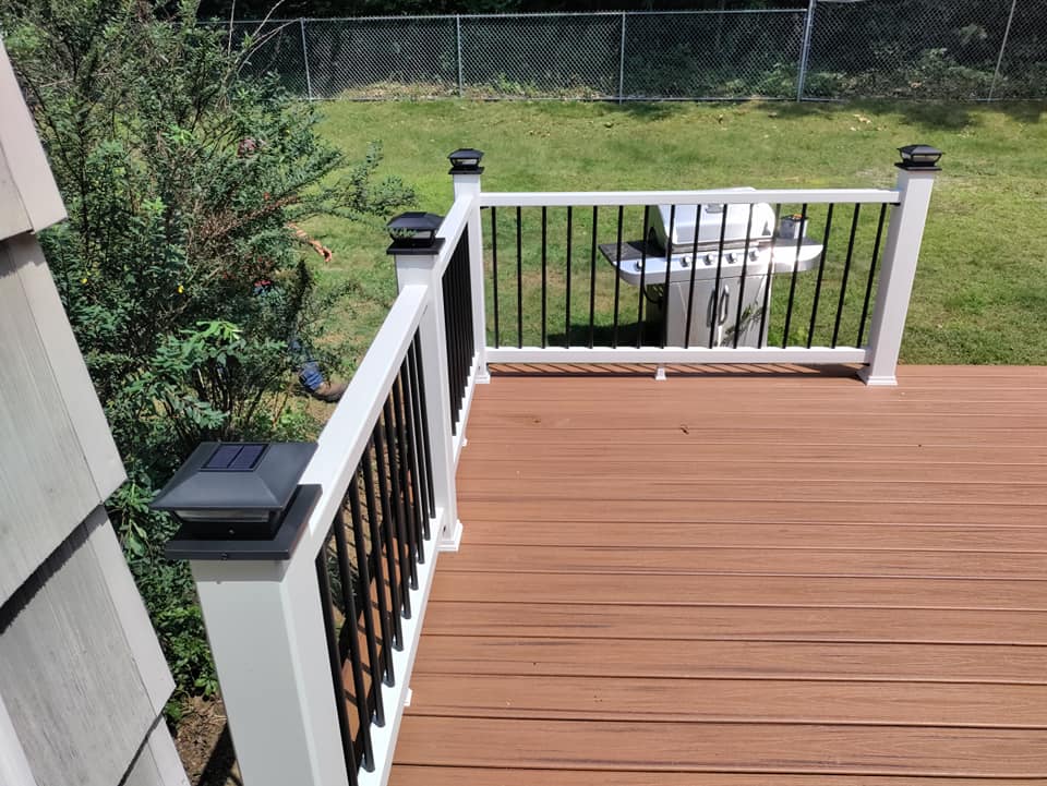 A wooden deck with a white railing and a fence in the background