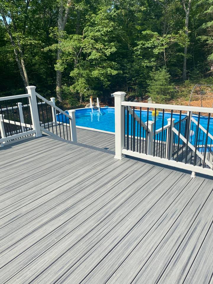 A gray deck with a white railing overlooking a swimming pool.