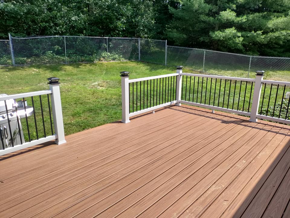 A wooden deck with a white railing and a fence in the background.