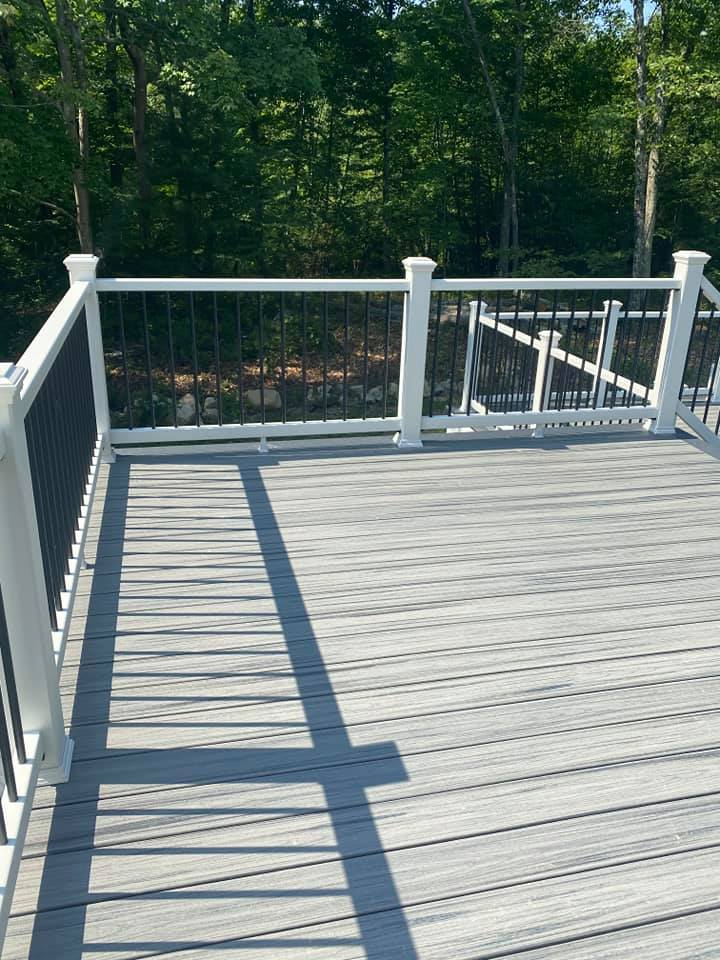 A wooden deck with a white railing and trees in the background.