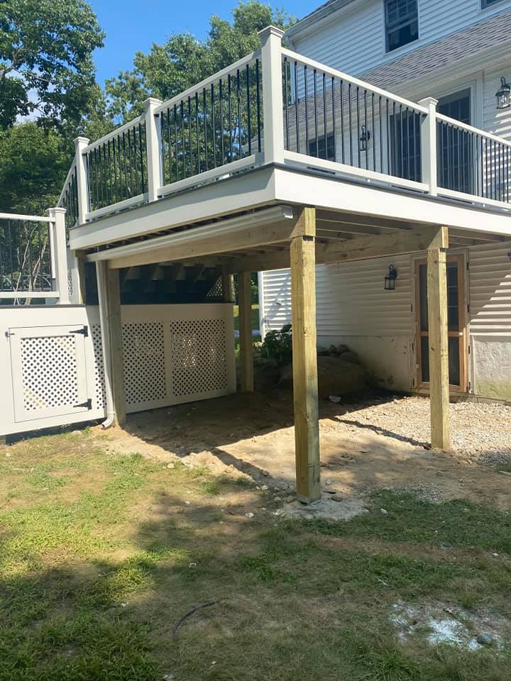 A white deck with a black railing is in the backyard of a house.