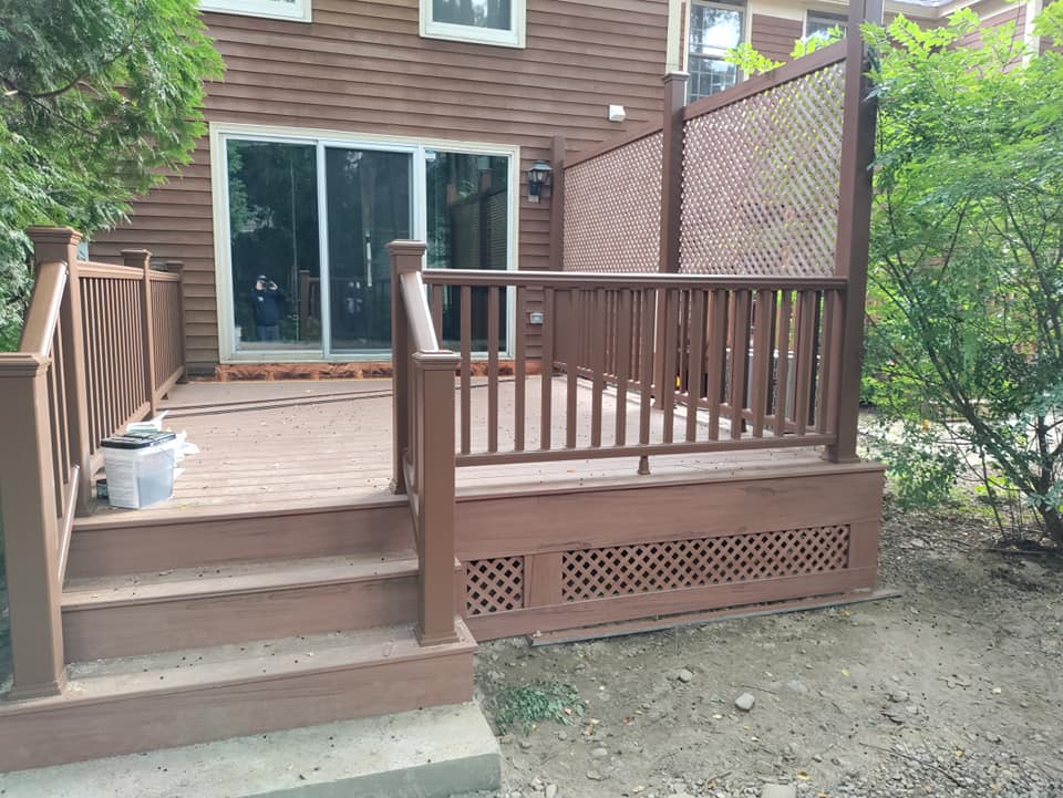 A wooden deck with stairs and a railing in front of a house.