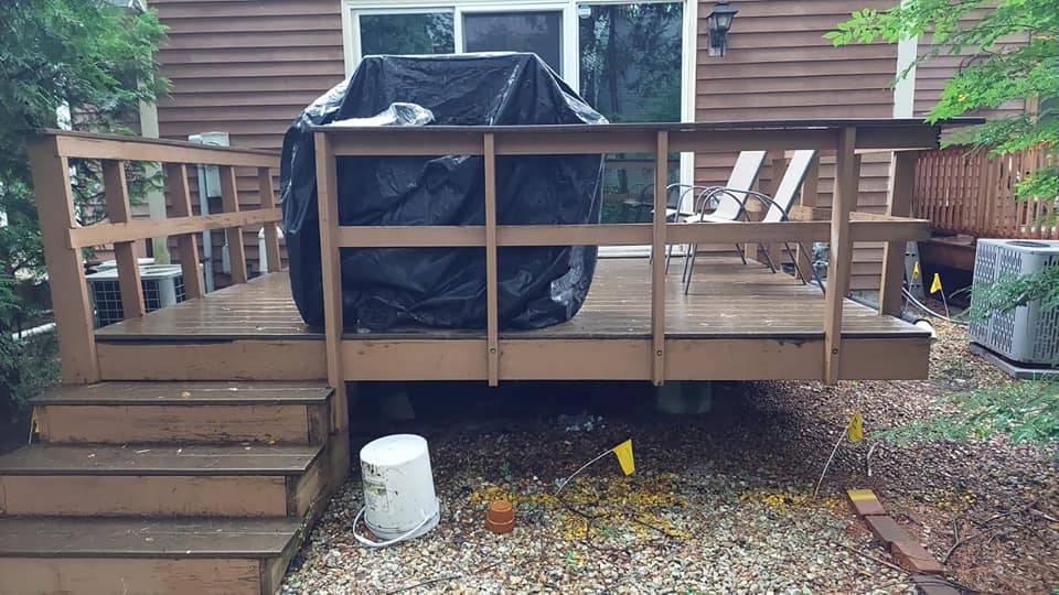 A wooden deck with stairs and a grill on it in front of a house.