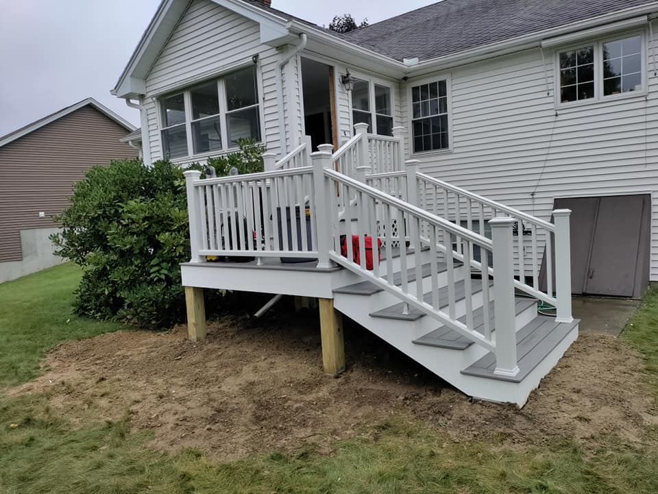 A white house with a deck and stairs in front of it.