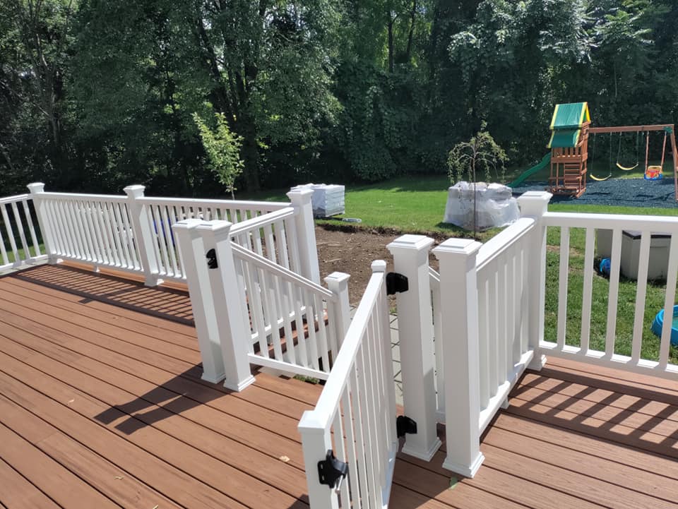A deck with a white railing and a swing set in the background.