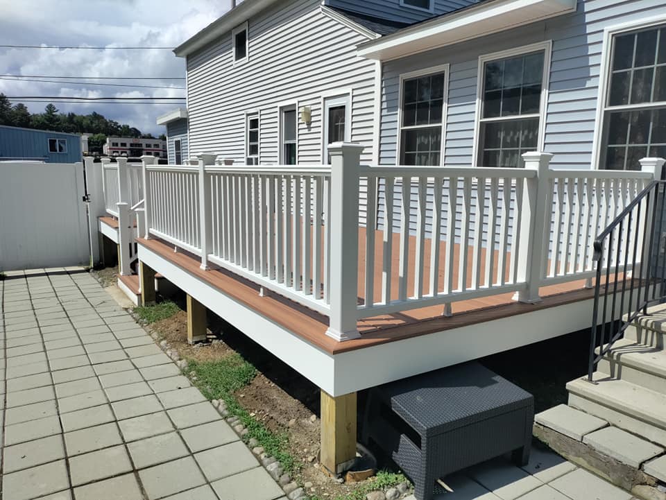 A large deck with a white railing is in front of a house.