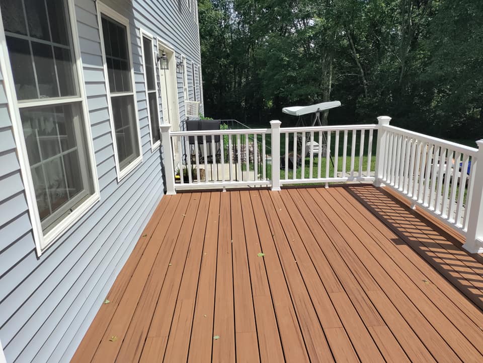 A wooden deck with a white railing and a blue house in the background