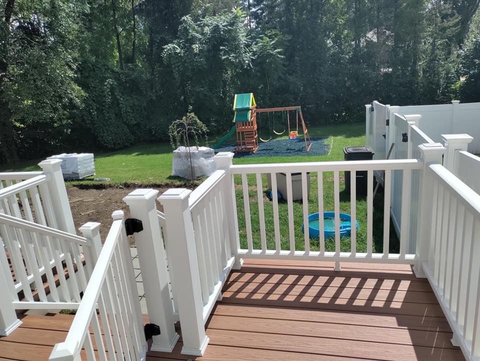 A deck with a white railing and a swing set in the background