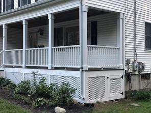 A white house with a porch and a fence in front of it.
