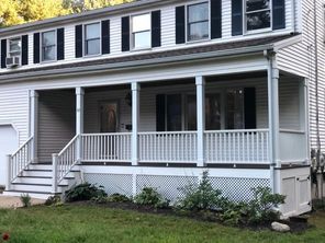 A white house with a large porch and black shutters.
