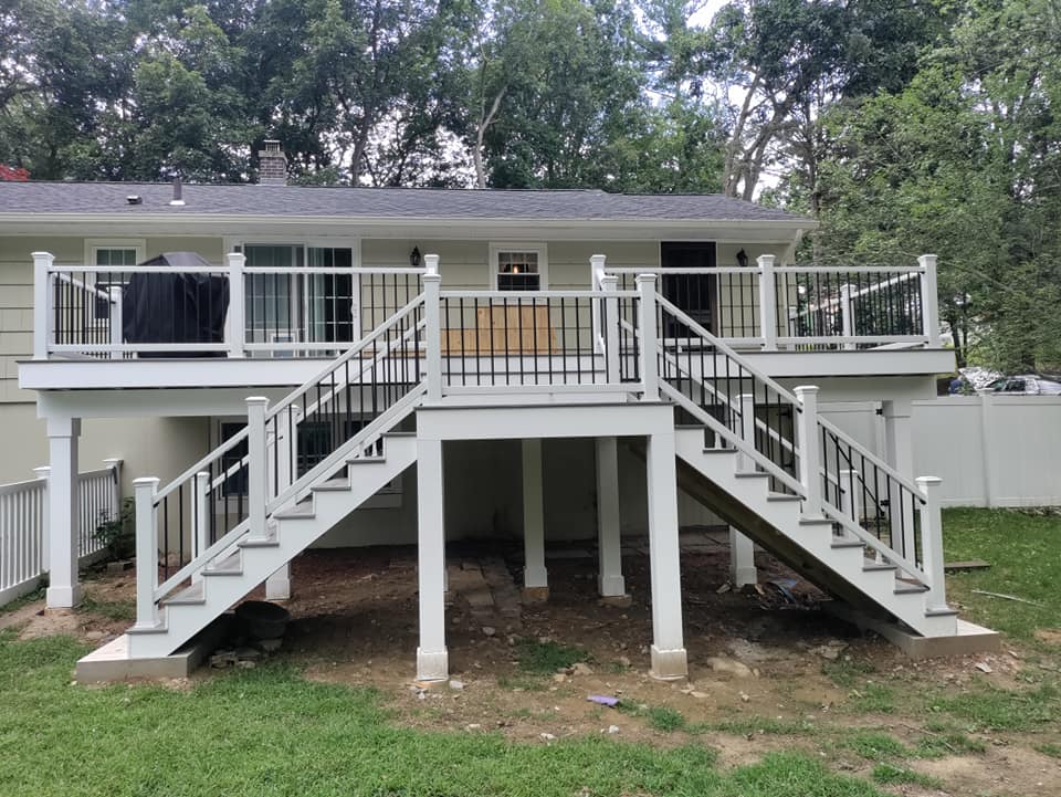 A white deck with stairs leading up to it is in the backyard of a house.