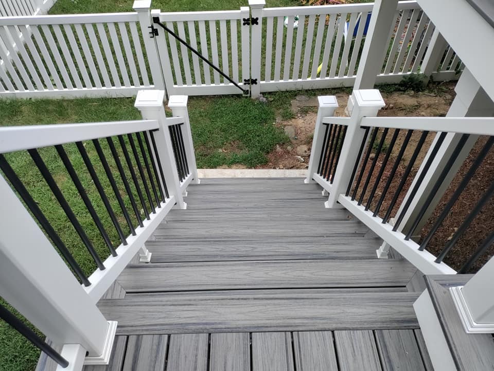 A staircase leading up to a deck with a white fence in the background.