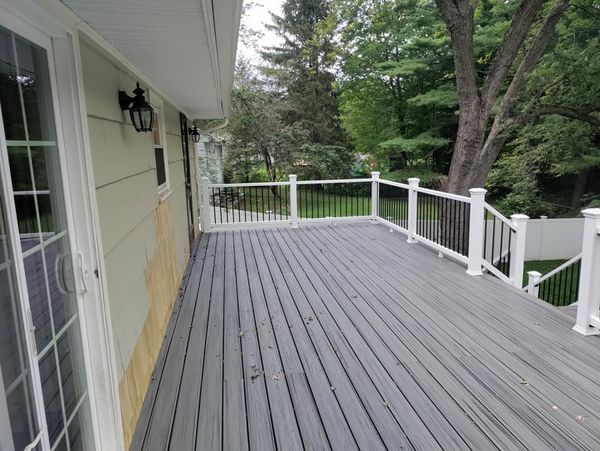 A large wooden deck with a white railing and stairs leading up to it.