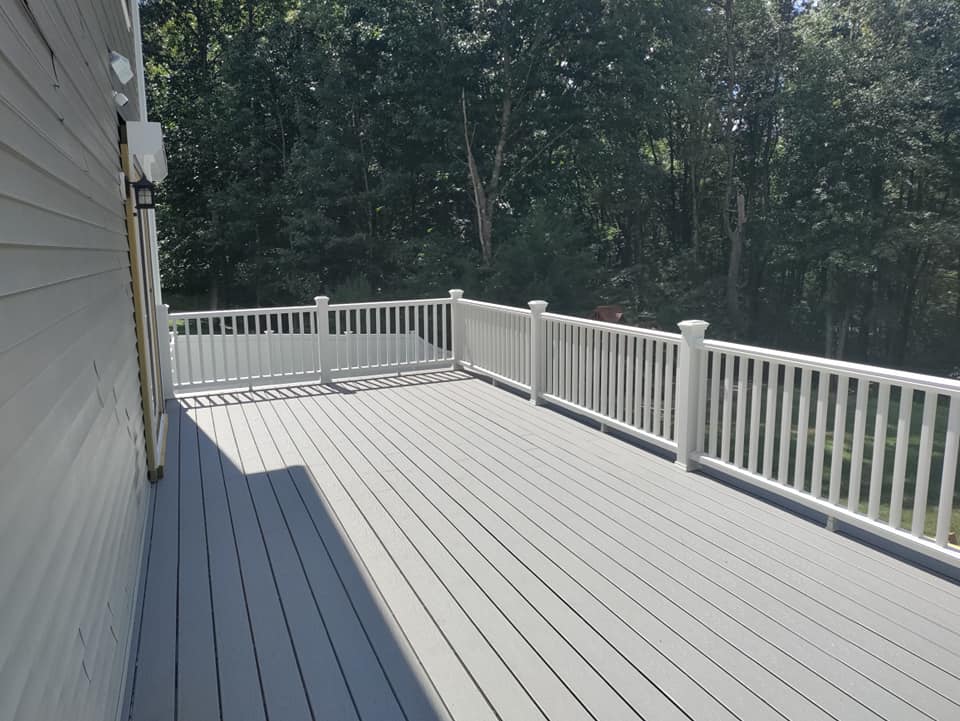 A large deck with a white railing and trees in the background