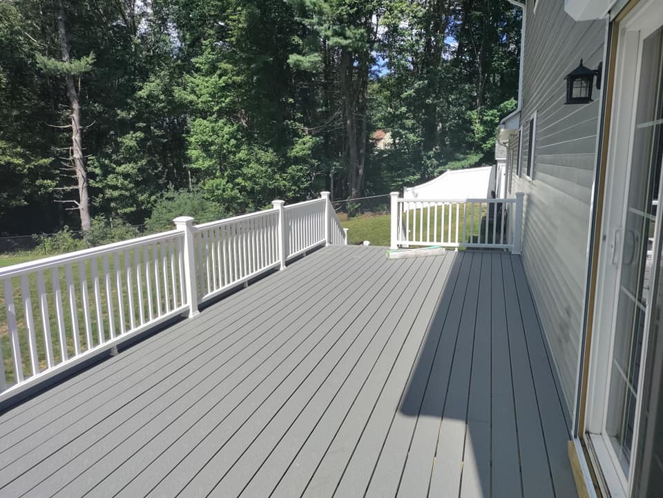 A large gray deck with a white railing and trees in the background.