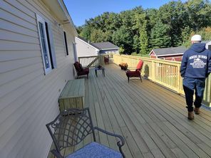 A man is walking on a wooden deck next to a house.
