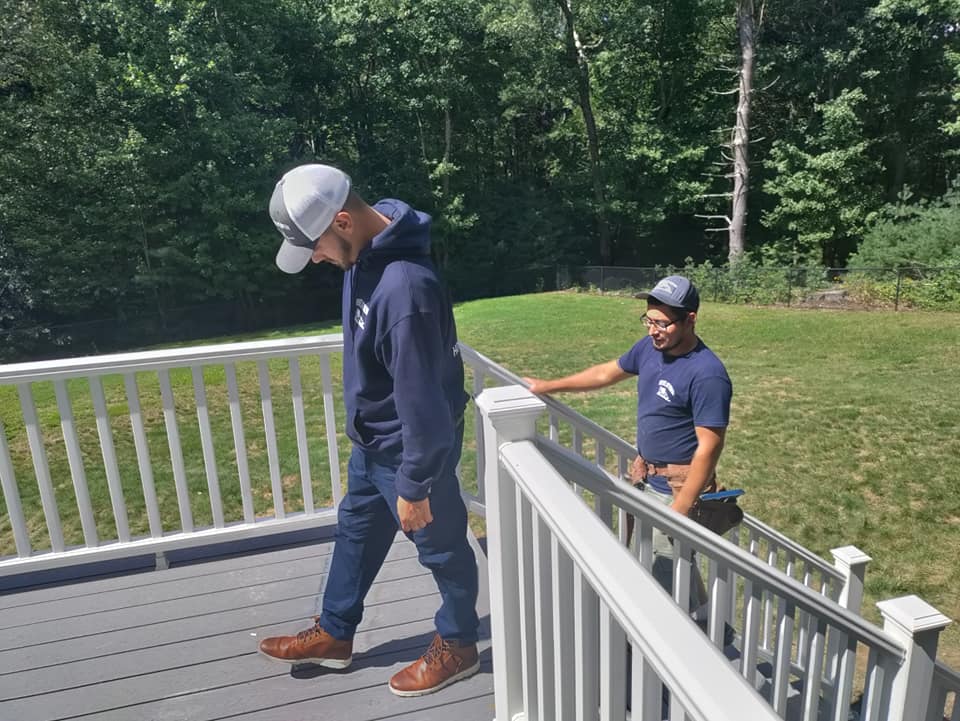 Two men are standing on a deck with a white railing.