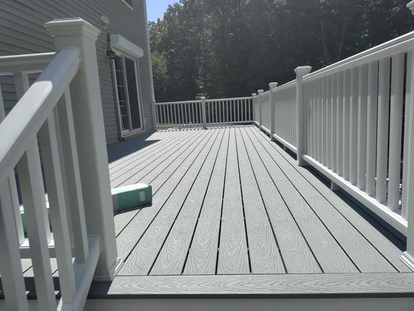 A gray deck with a white railing and a house in the background.