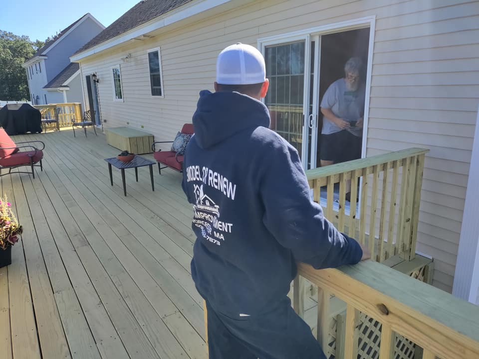 A man in a blue hoodie is leaning on a railing on a deck.