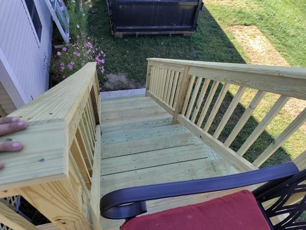 A person is standing on a wooden deck with stairs and a chair.