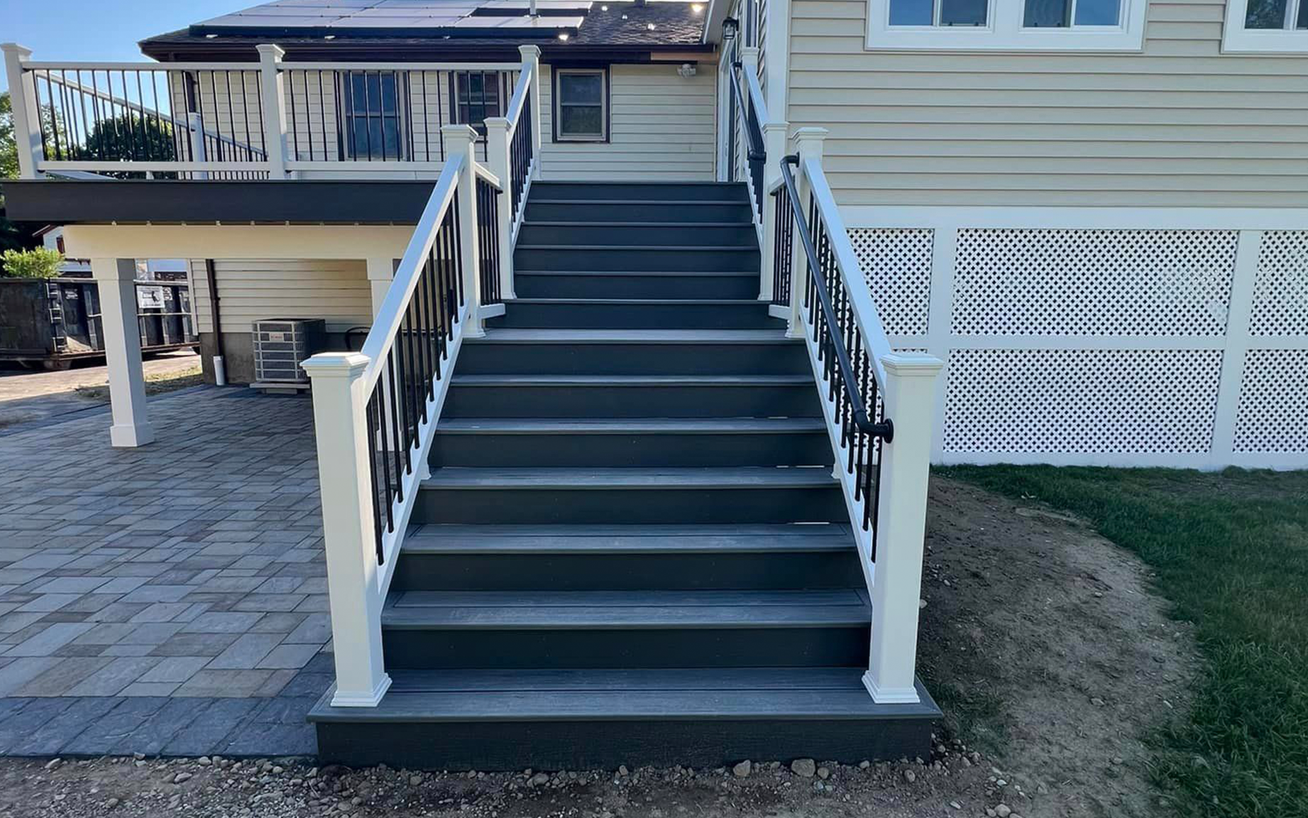 A large wooden deck with stairs leading up to it is in the backyard of a house.