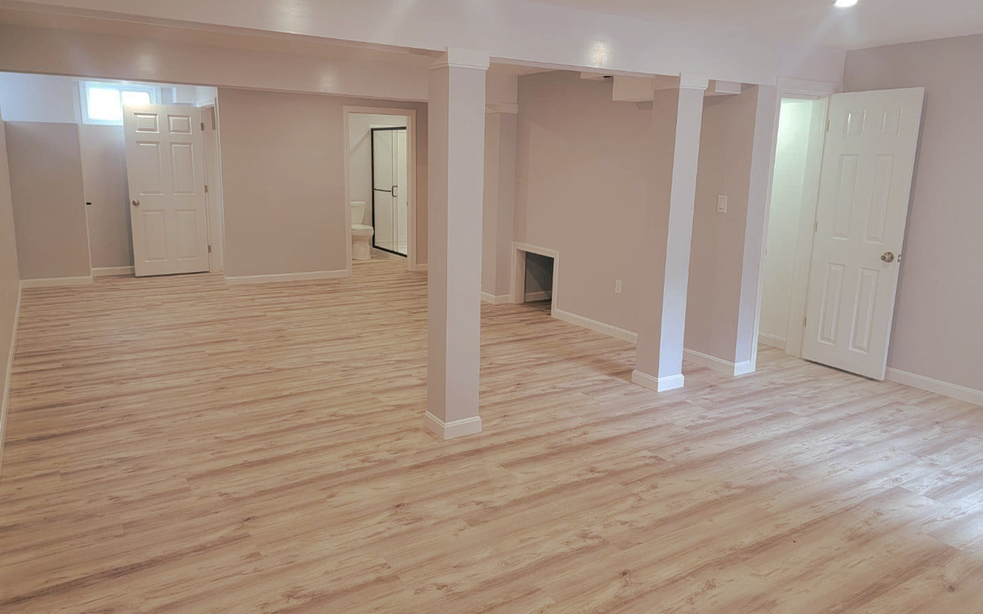 An empty basement with hardwood floors and white walls.