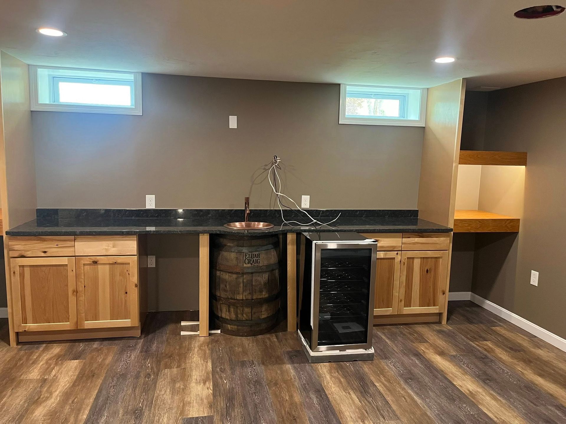 A basement with wooden cabinets, a sink, a barrel and a wine cooler