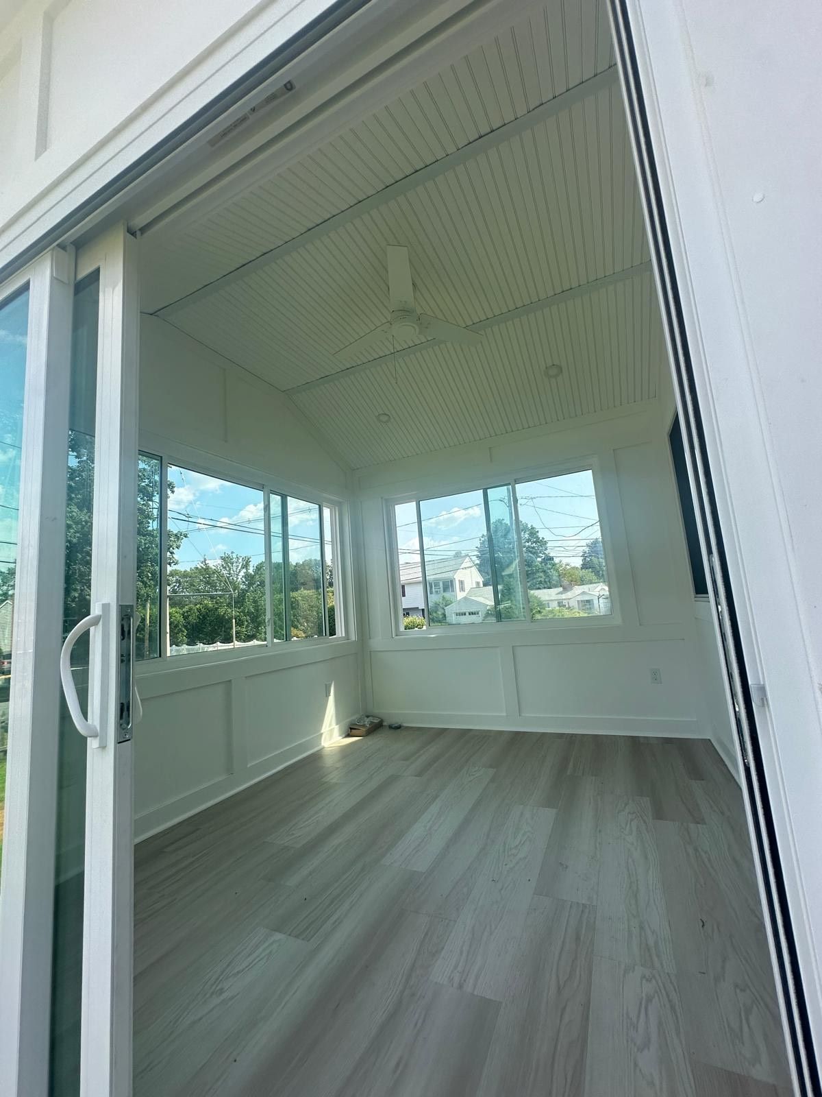 Bright sunroom with sliding glass door open, light grey floor, white walls, and large windows.