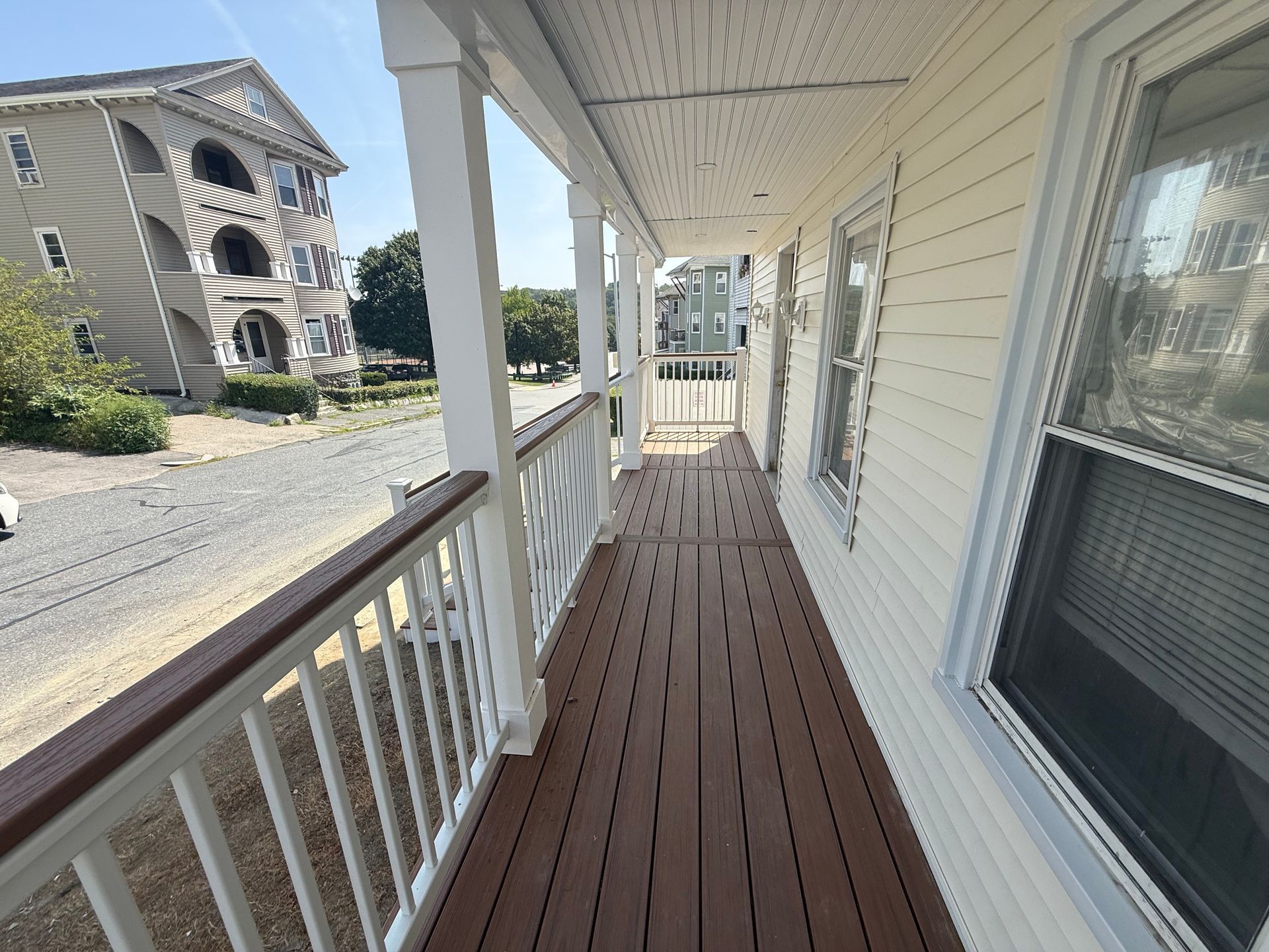 A long, narrow porch with brown decking and white railings, a building in the background.