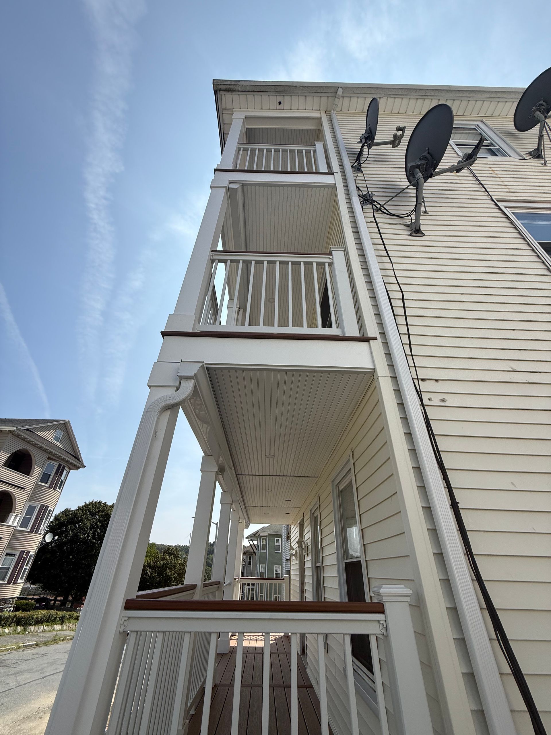 White multi-level porch on a building with satellite dishes against a blue sky.