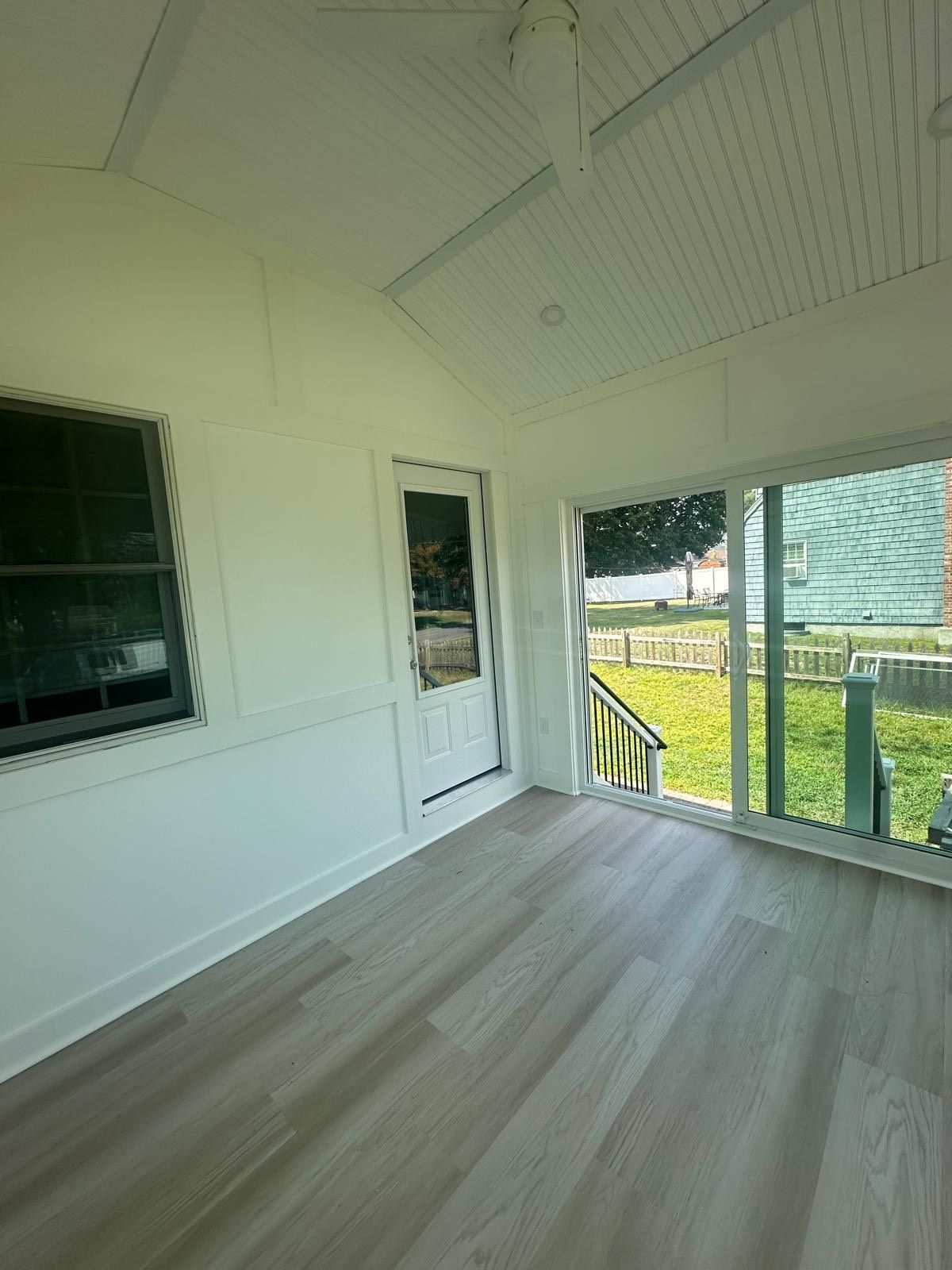 Sunroom with light wood-look flooring, white walls, a door, a window, and a glass sliding door to a yard.