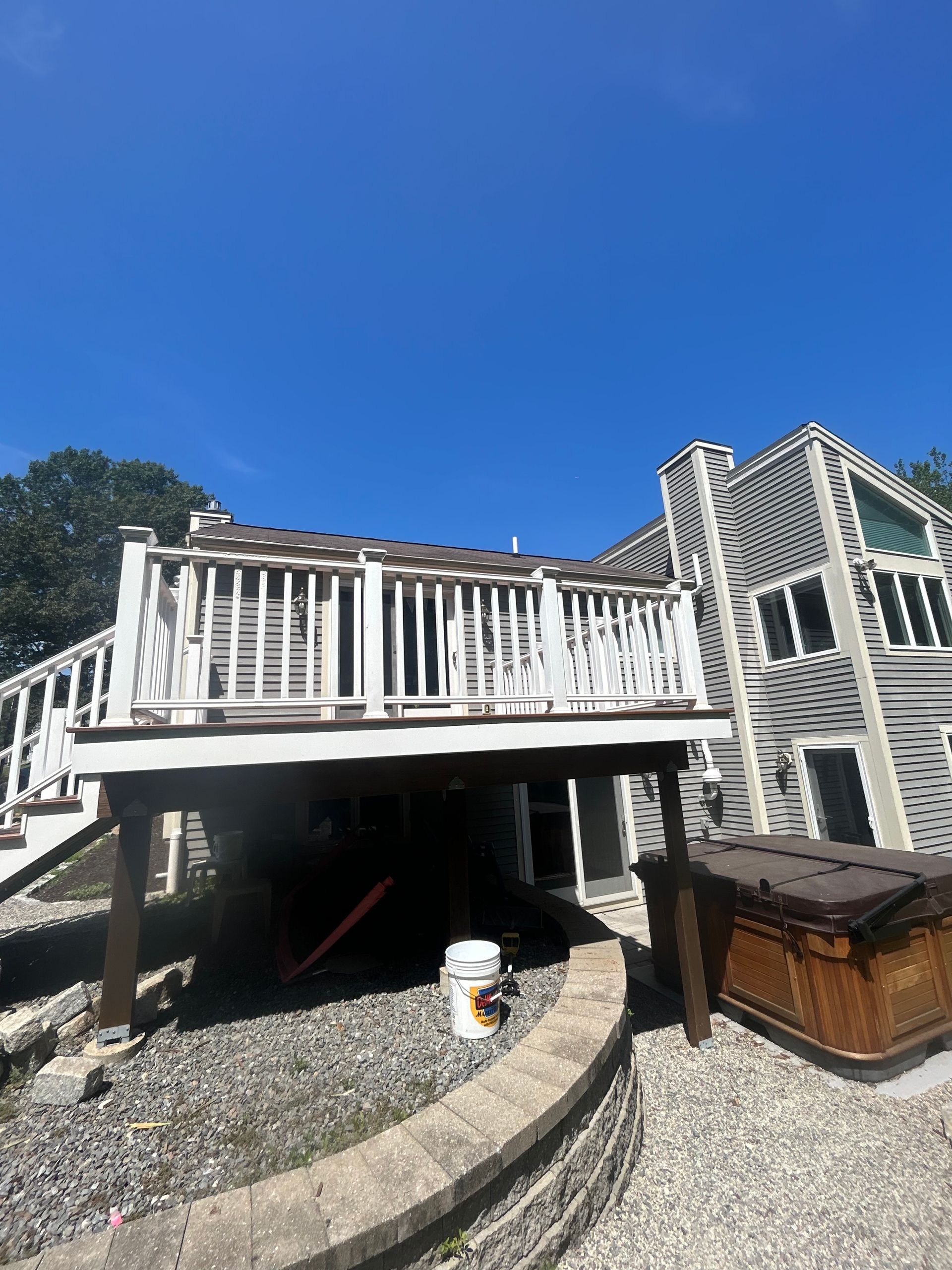 Wooden deck on a house with white railing, grey siding, and blue sky.