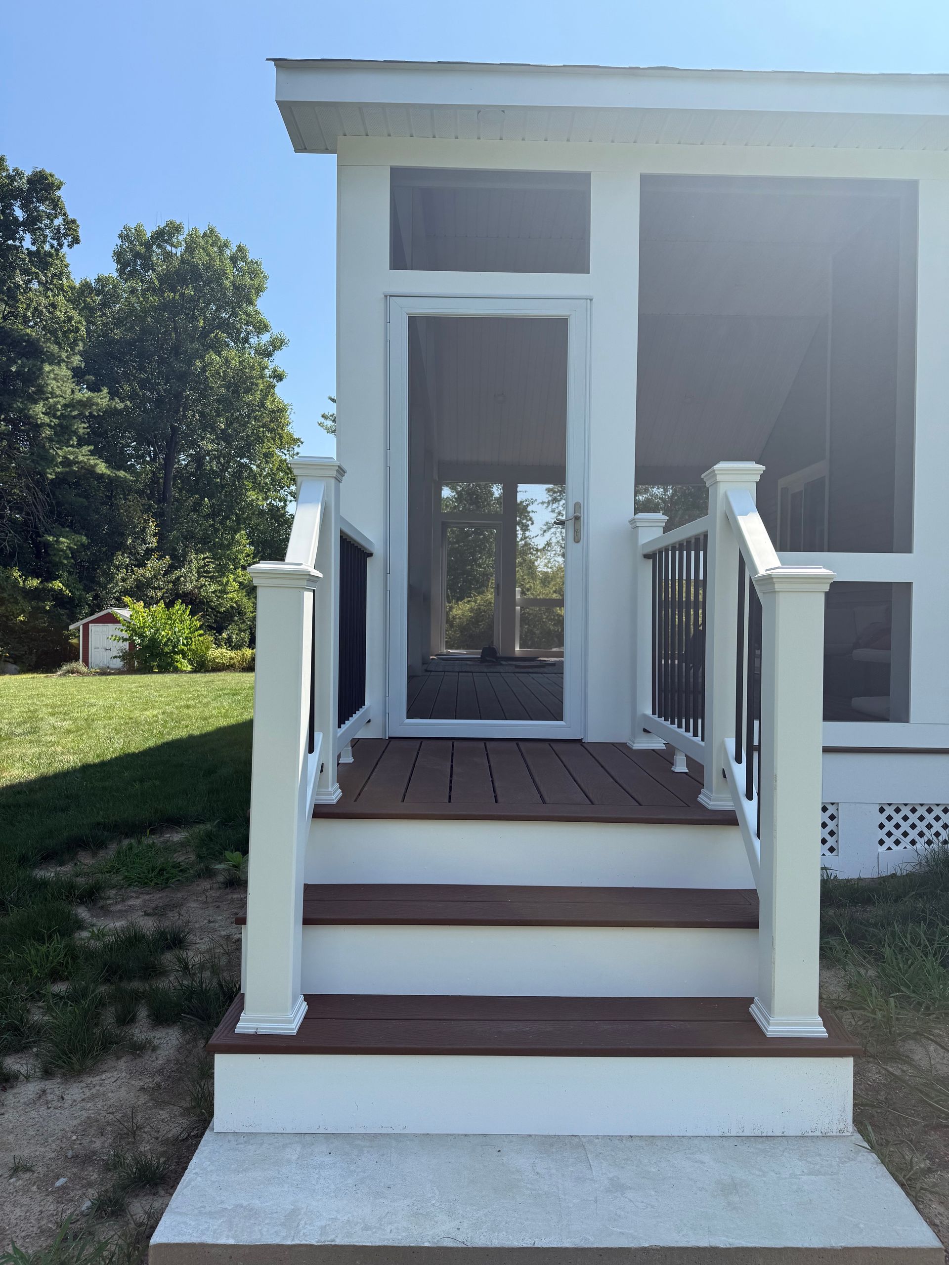 White porch with steps and a screened door; brown decking, white railings, and green lawn in the background.