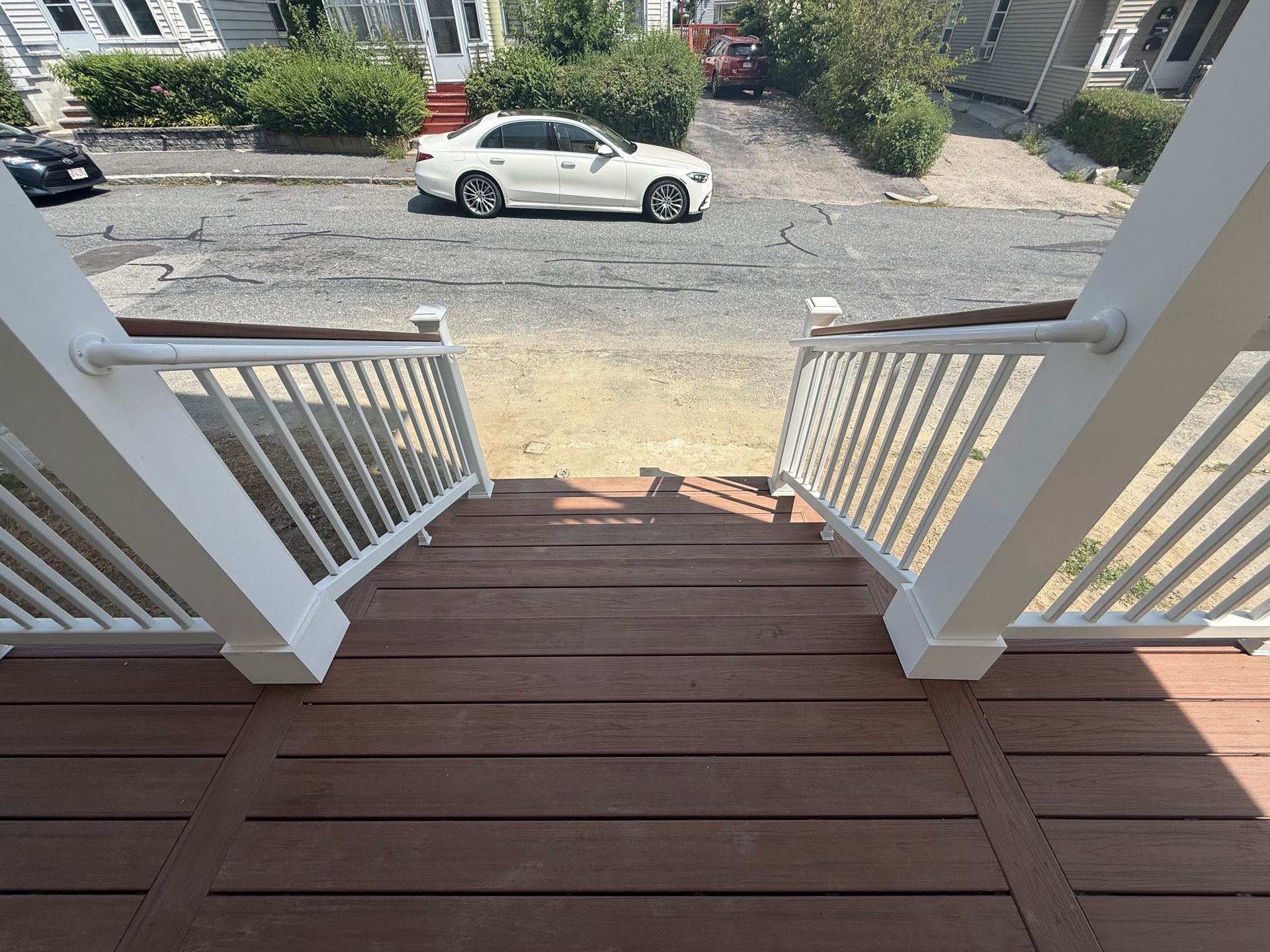 View from a porch down wooden steps to a street with parked cars.
