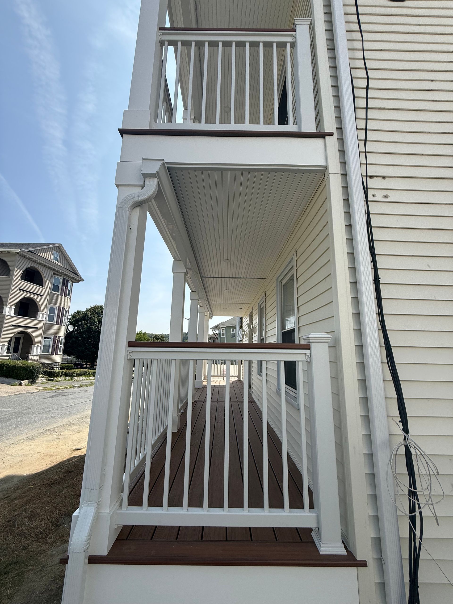 White porch with brown decking, overlooking a residential area under a blue sky.