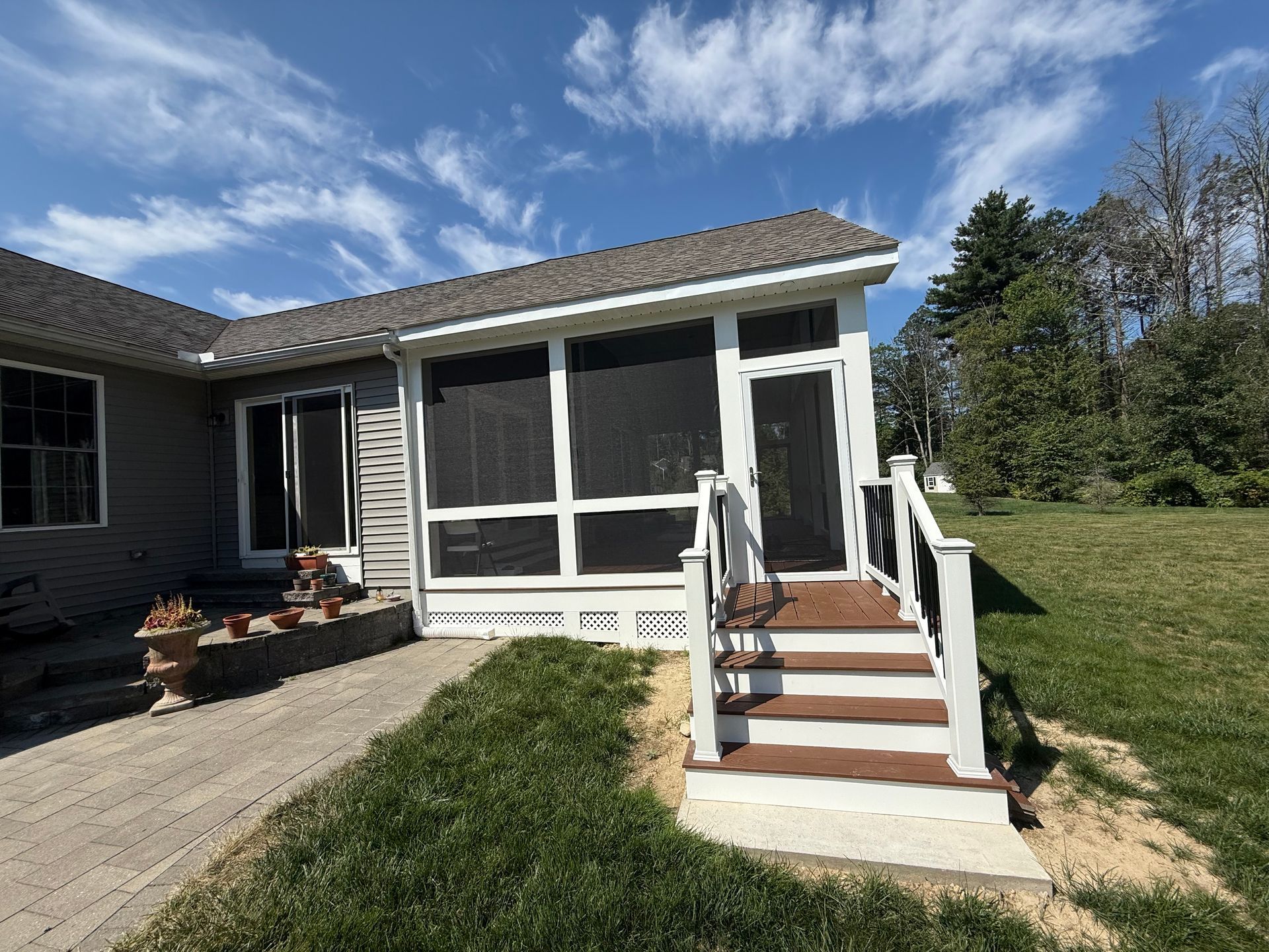 Screened porch with brown steps, white trim, and gray roof under a blue sky.
