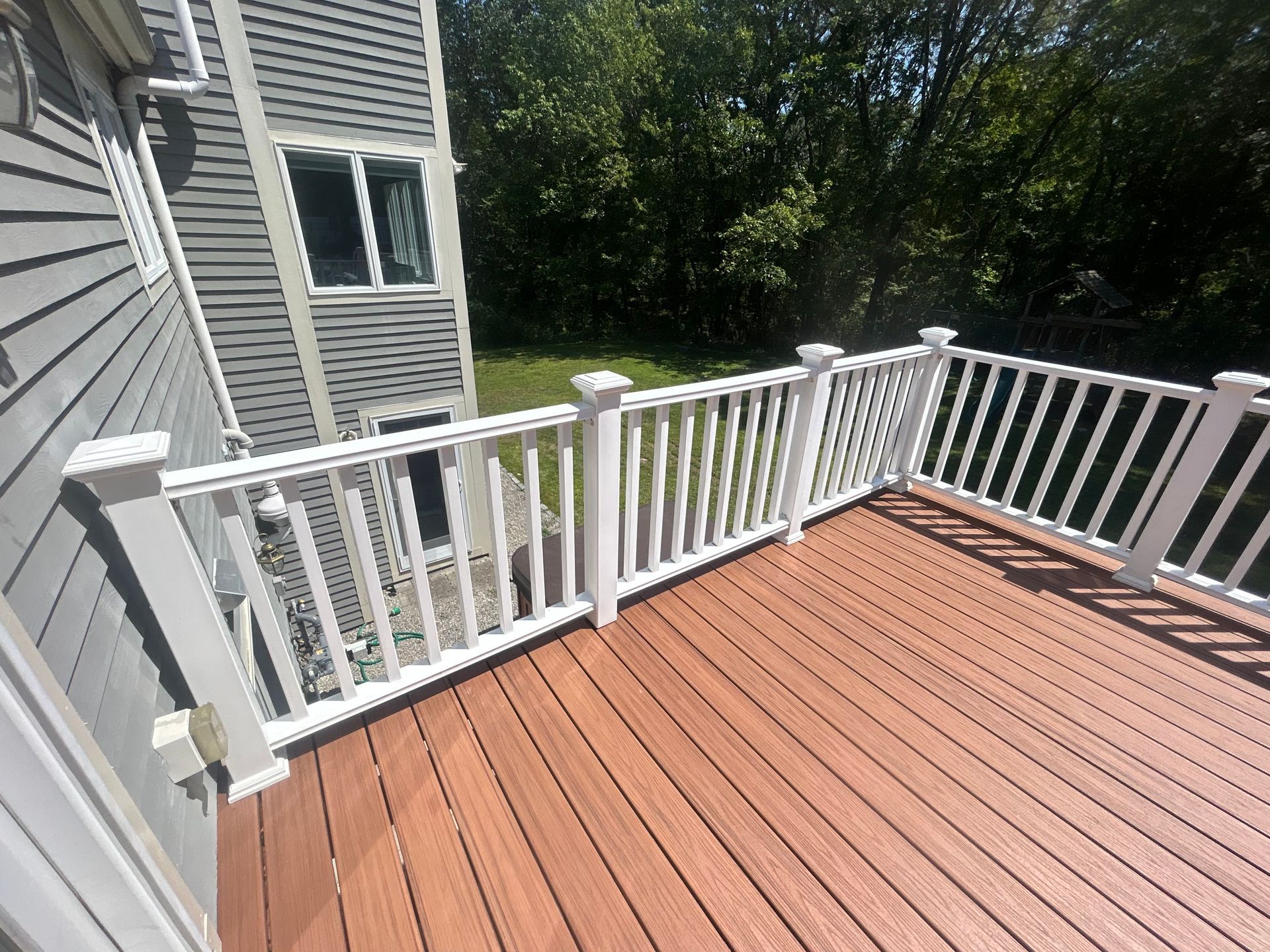 A composite deck with white railing, attached to a gray house, overlooking a yard.