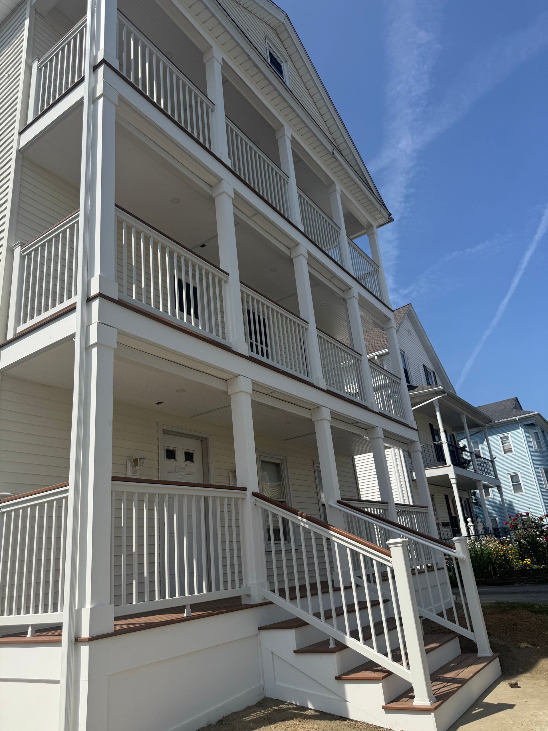 Three-story white building with multiple balconies and stairs, under a blue sky
