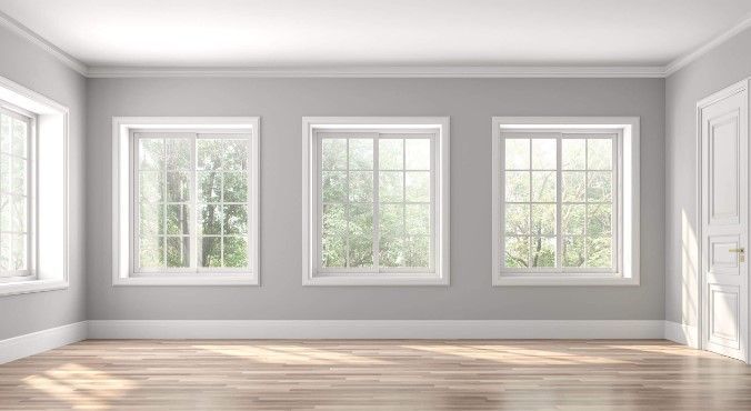An empty room with three windows and a wooden floor.