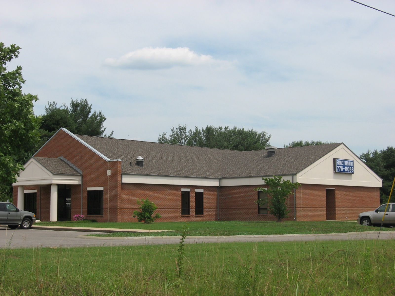 Single-story brick building with a blue sign, seen from across a road and grassy field