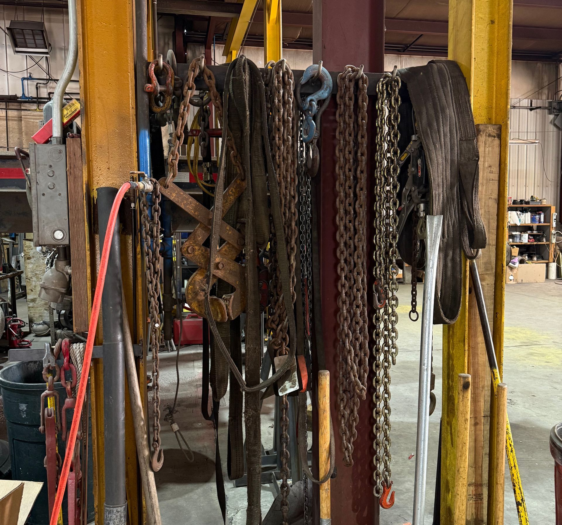 Chains, straps, and tools hang on a yellow pole in a garage, showing wear and tear.